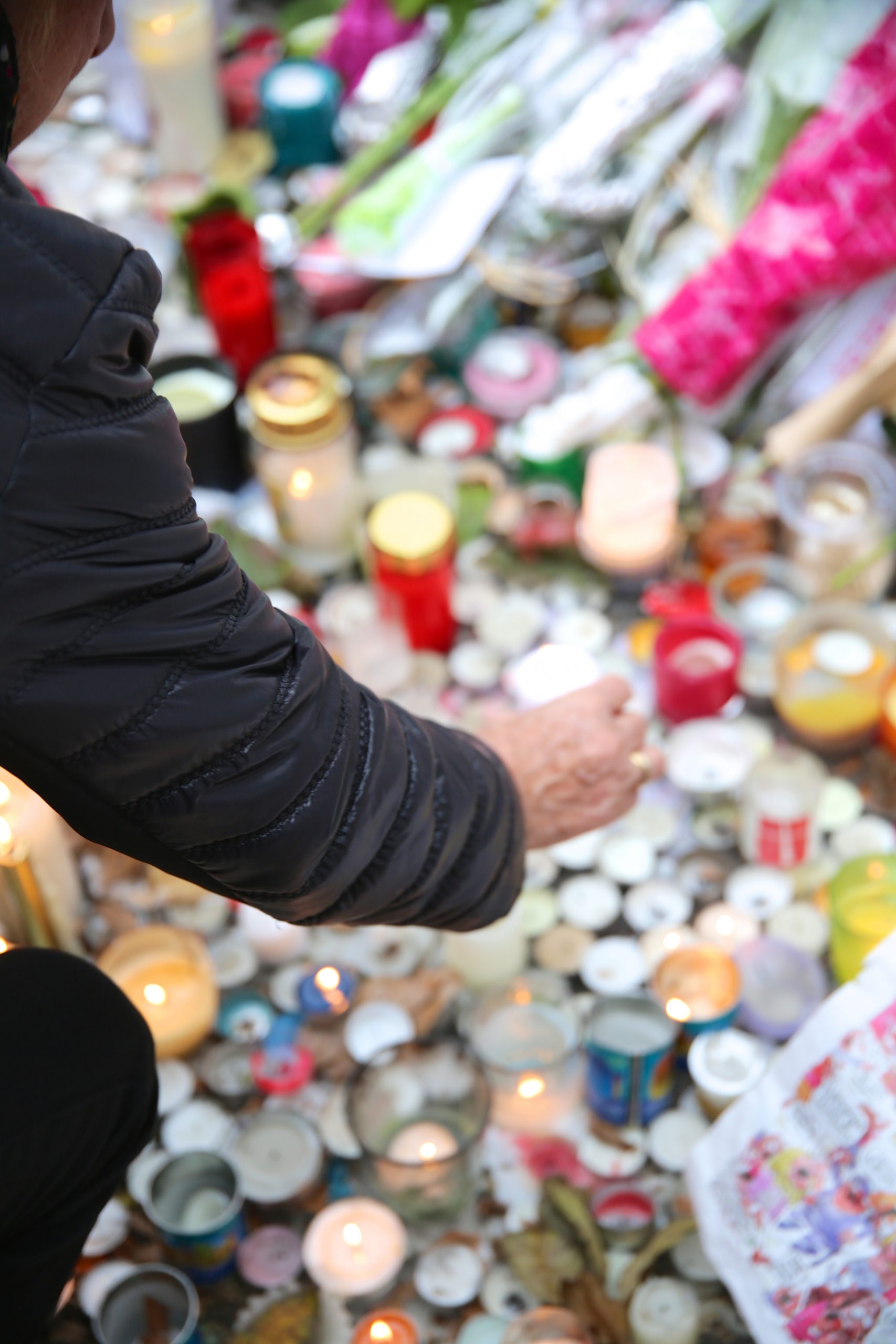 Paris, France - November 29, 2015: A woman reaches down to light at candle at the memorial at the Theater Le Bataclan for the victims of the November 13, 2015 terrorist attack in Paris, France.